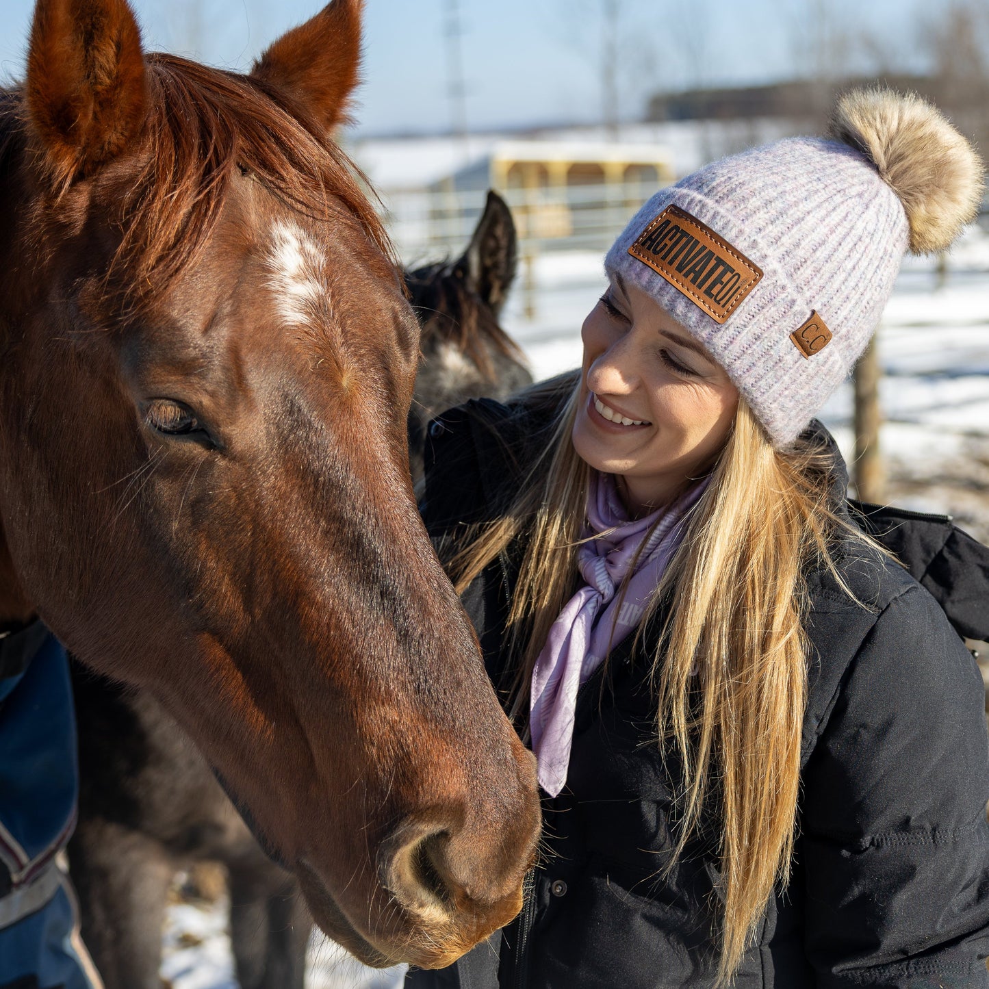 Woman wearing an ActivateQi beanie smiling with a horse outdoors in winter.