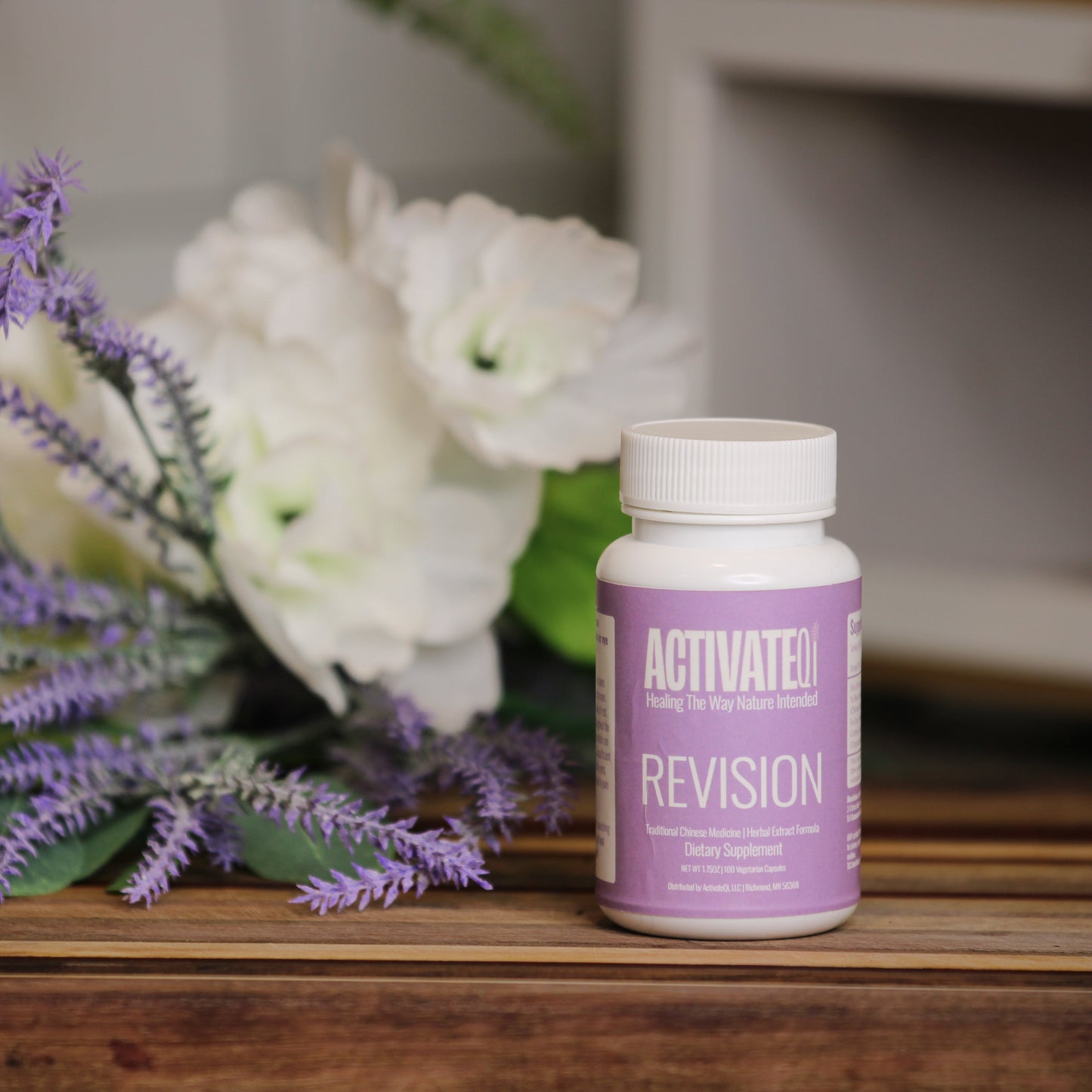 Bottle of ActivateQi Revision supplement on a wooden surface with flowers in the background