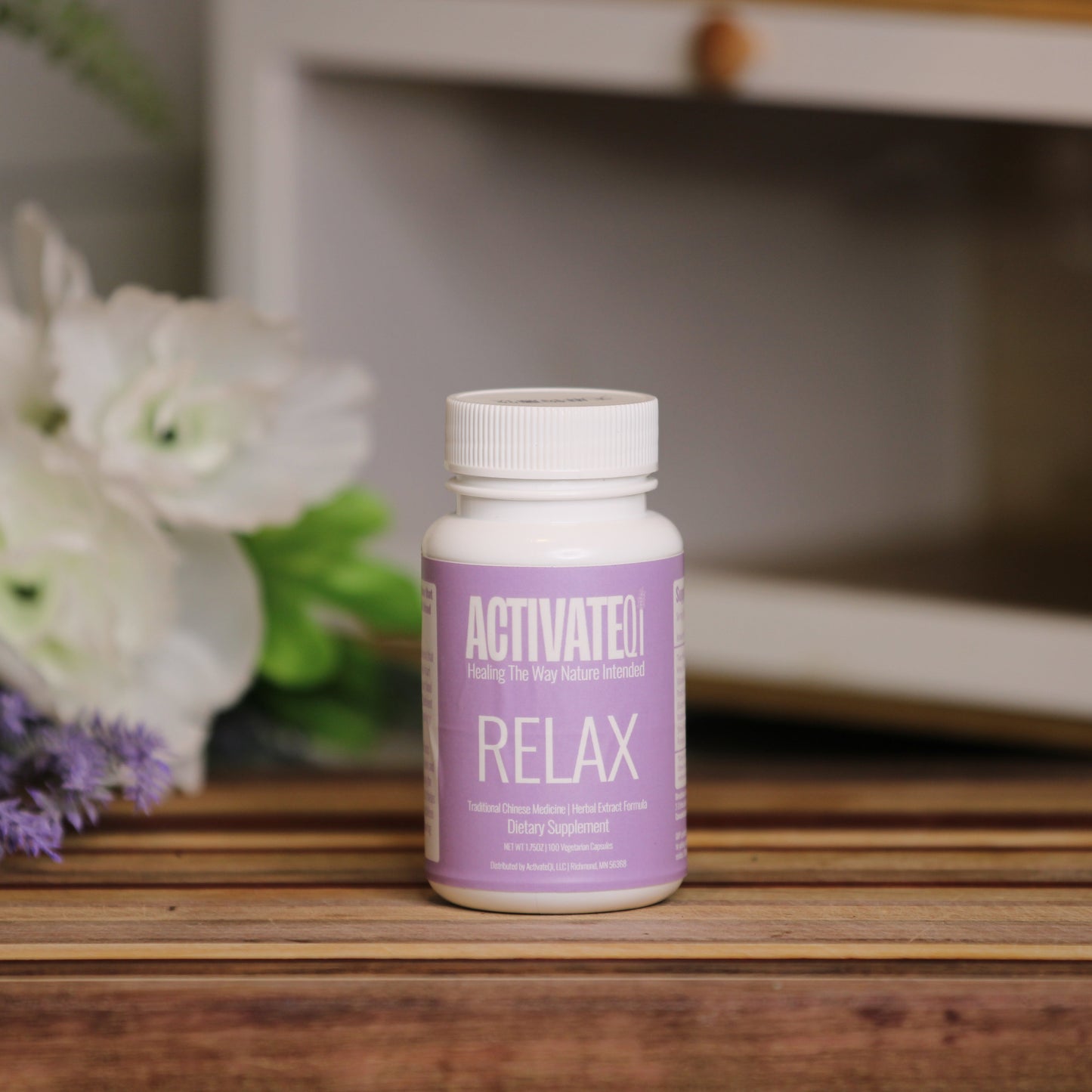Bottle of ActivateQi Relax supplement on a wooden surface with flowers in the background