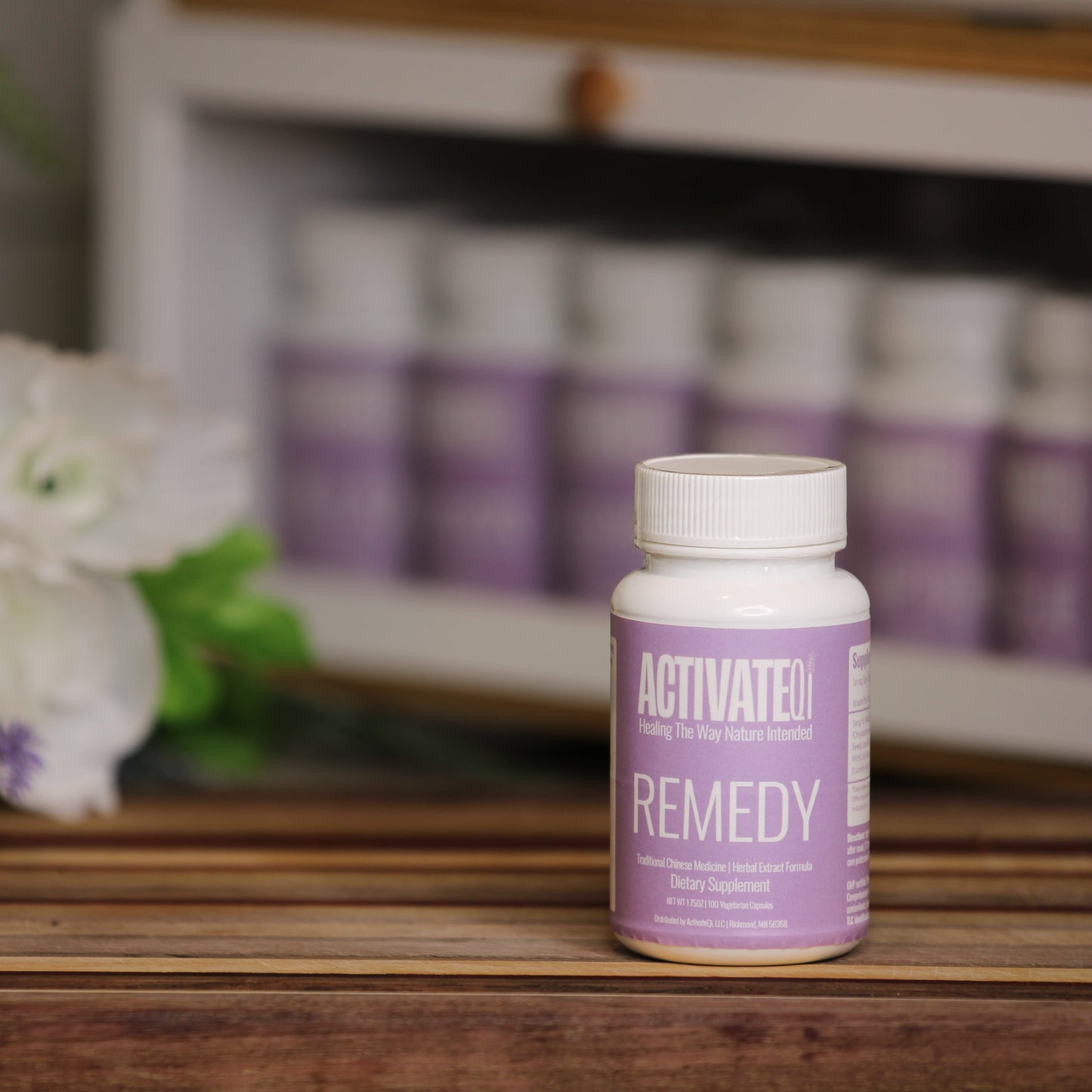 ActivatedQi Remedy bottle on a wooden surface with flowers and more bottles in the background