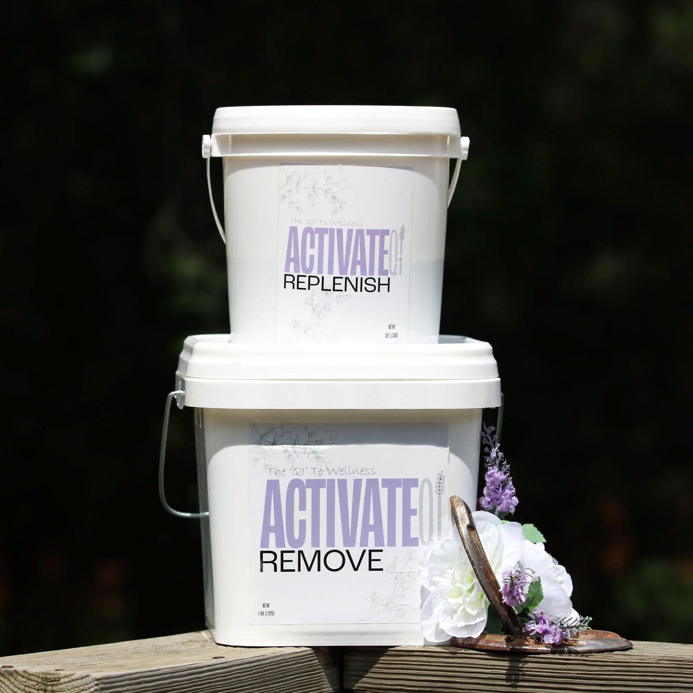 Two white buckets labeled ActivateQi, 'Replenish', and 'Remove' on a wooden surface with a blurred natural background.