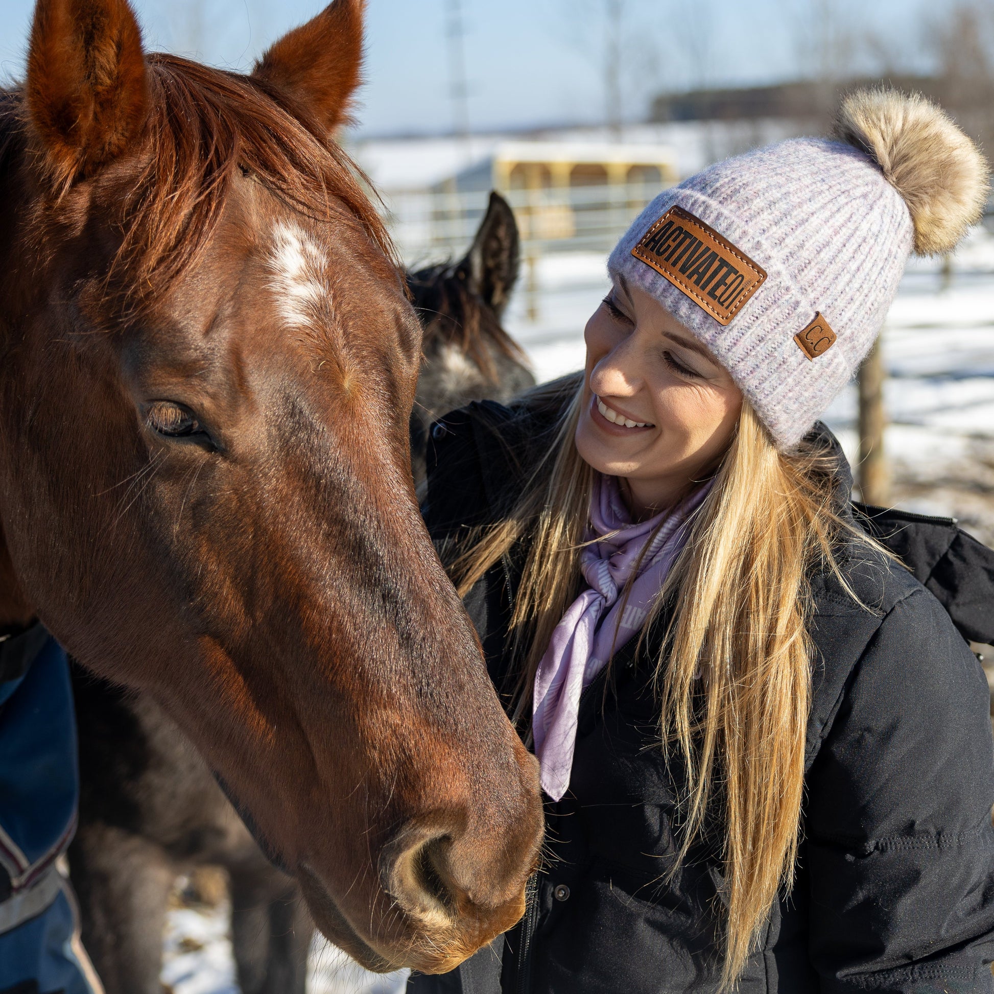 Woman wearing an ActivateQi beanie smiling with a horse outdoors in winter. 
