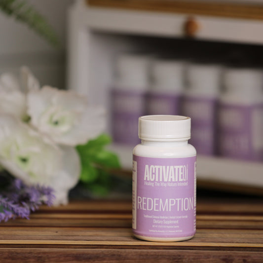 Purple bottle labeled ActivateQi Redemption on a wooden surface with flowers in the background