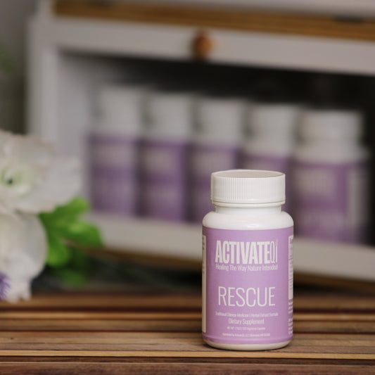 Bottle of ActivateQi Rescue on a wooden surface with flowers and more bottles in the background.