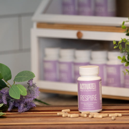 ActivateQi Respire supplement bottle with pills on a wooden surface with plants in the background